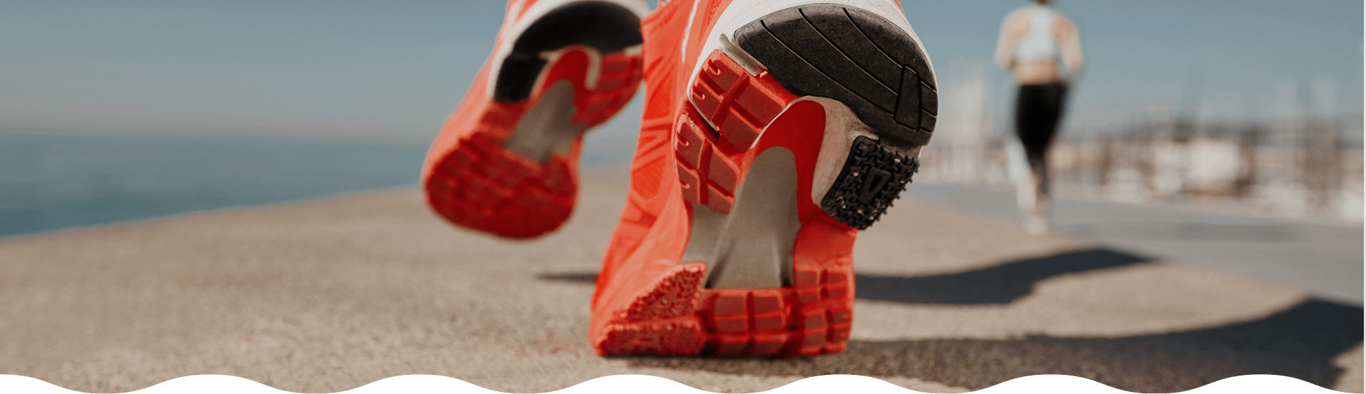 Close-up of red running shoes with a blurred background of a person running on a path.