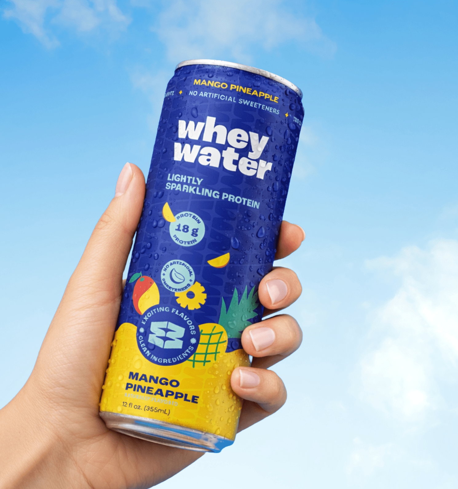 Hand holding a can of Whey Water Mango Pineapple flavor against a blue sky background